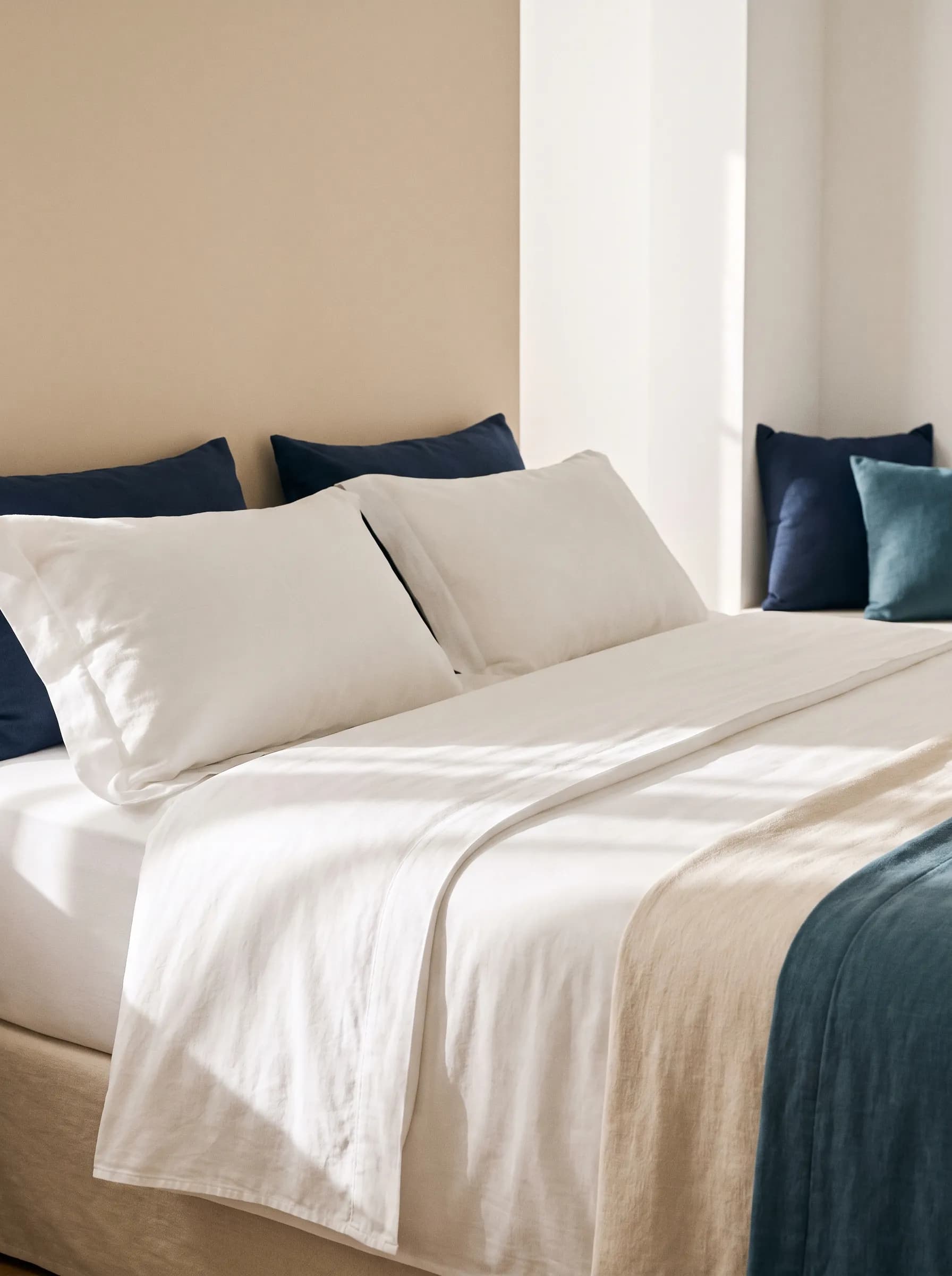 Cama de hotel vestida con ropa de cama blanca de algodón y cojines azul marino